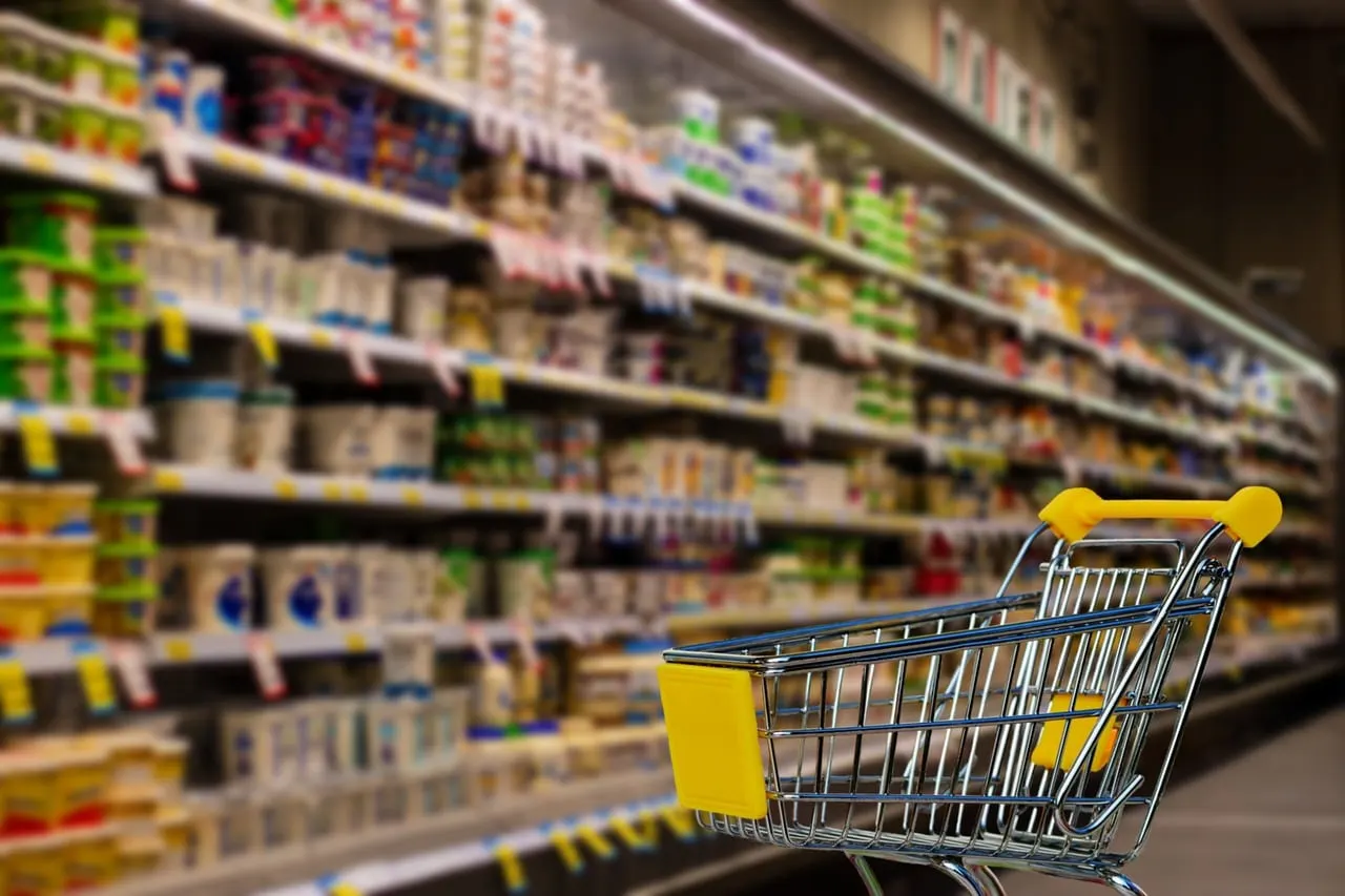 Shopping trolley in a supermarket aisle with well-stocked shelves